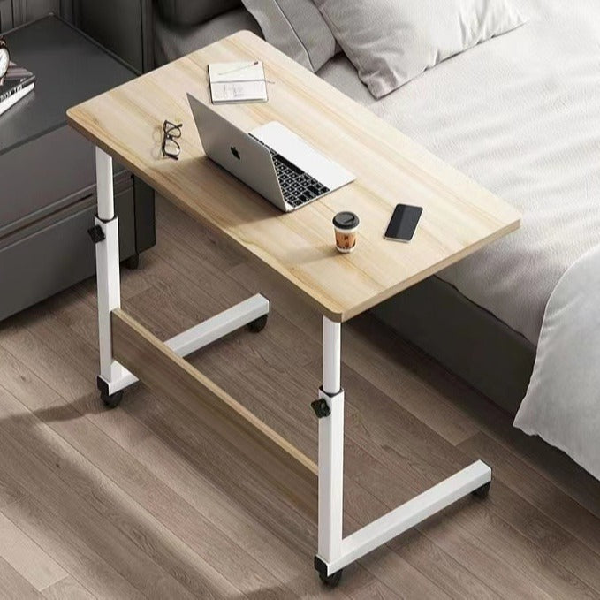 Adjustable height desk with wheels next to bed, ideal for home offices, bedrooms, and versatile workspaces. Perfect for bulk furniture purchasing from China.