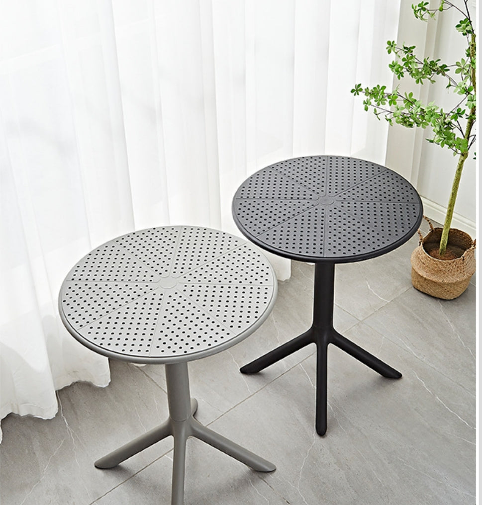 Two modern, round coffee tables with perforated tops placed in a well-lit indoor setting near a plant. Ideal for both indoor and outdoor use, highly practical for cafés, patios, and offices. Perfect for bulk purchasing directly from a Chinese manufacturer, offering versatility for various spaces.