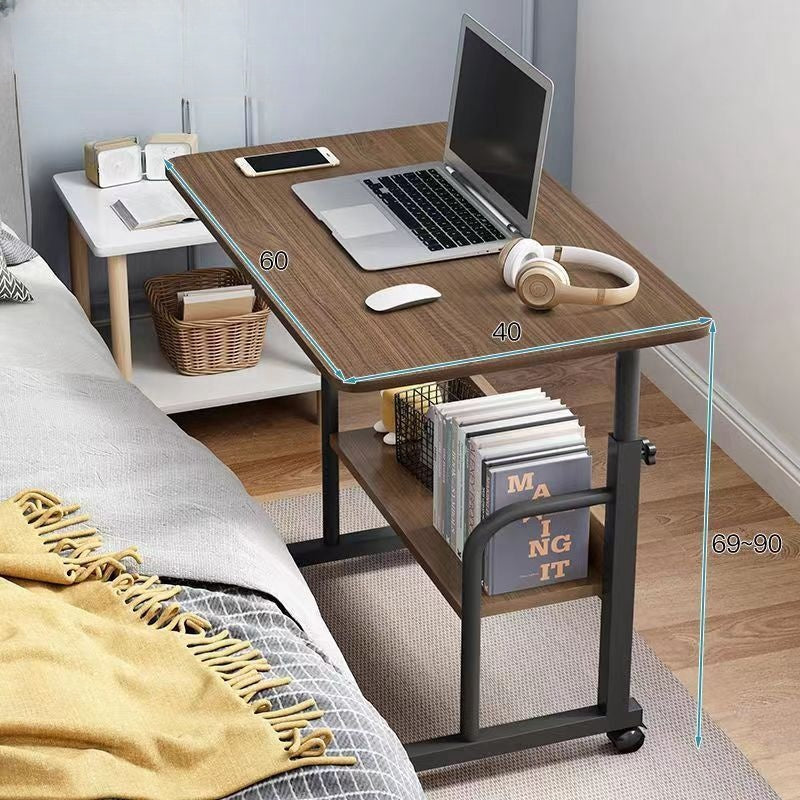 Adjustable mobile desk with shelf beside bed, holding a laptop, headphones, keyboard, and books, ideal for home office or bedroom use, showcasing flexibility and convenient wholesale sourcing directly from China.