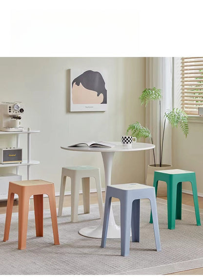 Stackable stools around a round dining table in a modern indoor setting, ideal for café seating, kitchens, or homes. Perfect for bulk purchasing directly from China with customization options for various spaces.