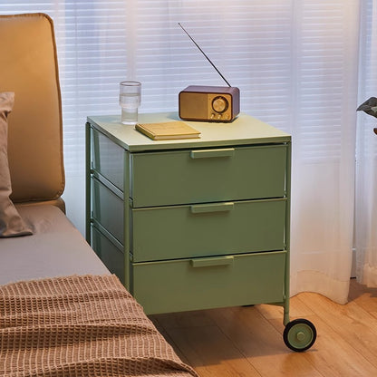 Bedside table with three drawers and smooth-rolling wheels positioned next to a bed in a cozy bedroom setting. Ideal for versatile storage and home organization, available for wholesale directly from China.